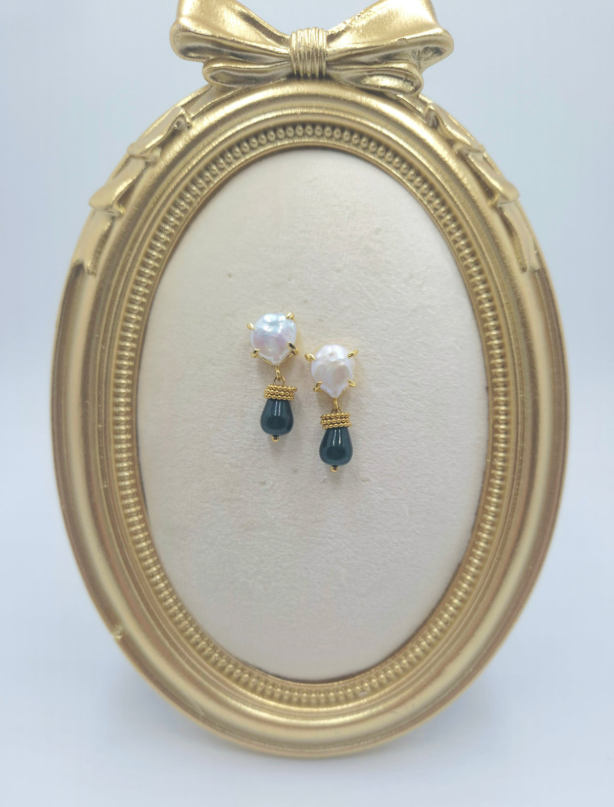 Close-up of pearl cushion studs, deep sea green-blue stone drops, and gold-tone rings